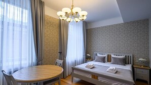 A hotel room with a bed, a round dining table, chairs, a chandelier, and curtains. - Roze Kūrmājas Residence (Liepaja)