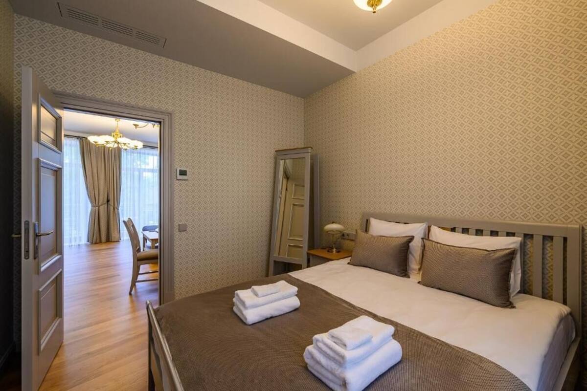 Habitación de hotel con cama, espejo, mesita de noche y vista a un comedor a través de una puerta abierta.