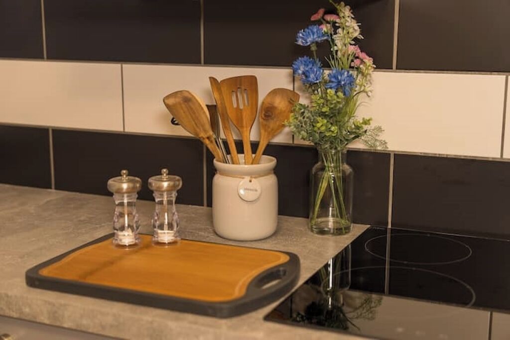 En køkkenbordplade med træredskaber, salt- og peberkværke samt en vase med blomster.