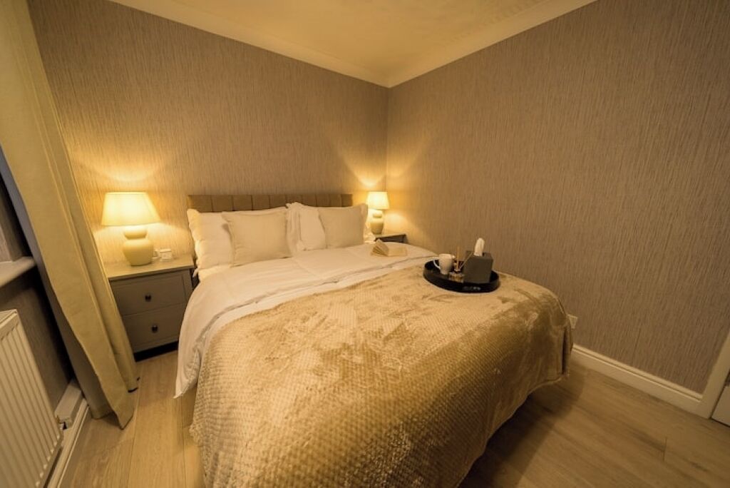 A bedroom with a bed, two bedside lamps, a nightstand, and a tray with a cup and a book.