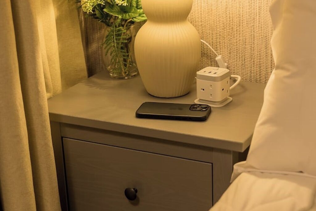 Een nachtkastje met een lamp, een stekkerdoos en een smartphone.