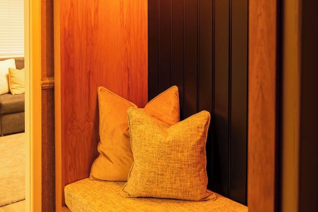 A corner of a room with a wooden panel and a cushioned bench with two pillows.