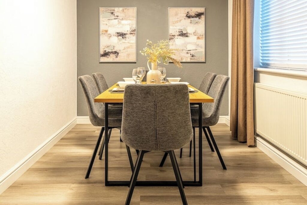 A dining area with a wooden table, four grey upholstered chairs, and two abstract paintings on the wall.
