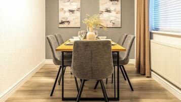 A dining area with a wooden table, four grey upholstered chairs, and two abstract paintings on the wall.