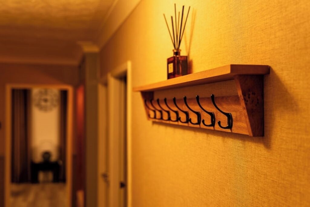 A hallway with a wooden shelf holding a reed diffuser and hooks.
