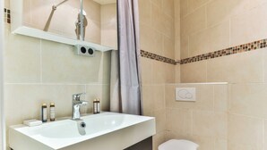 Een badkamer met een wit wastafelmeubel, spiegel en toilet. Op het aanrecht staan twee flessen.