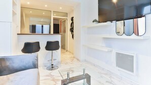 Een moderne woonkamer met een grote flatscreen televisie aan de muur, een bank, twee zwarte stoelen en een marmeren vloer.