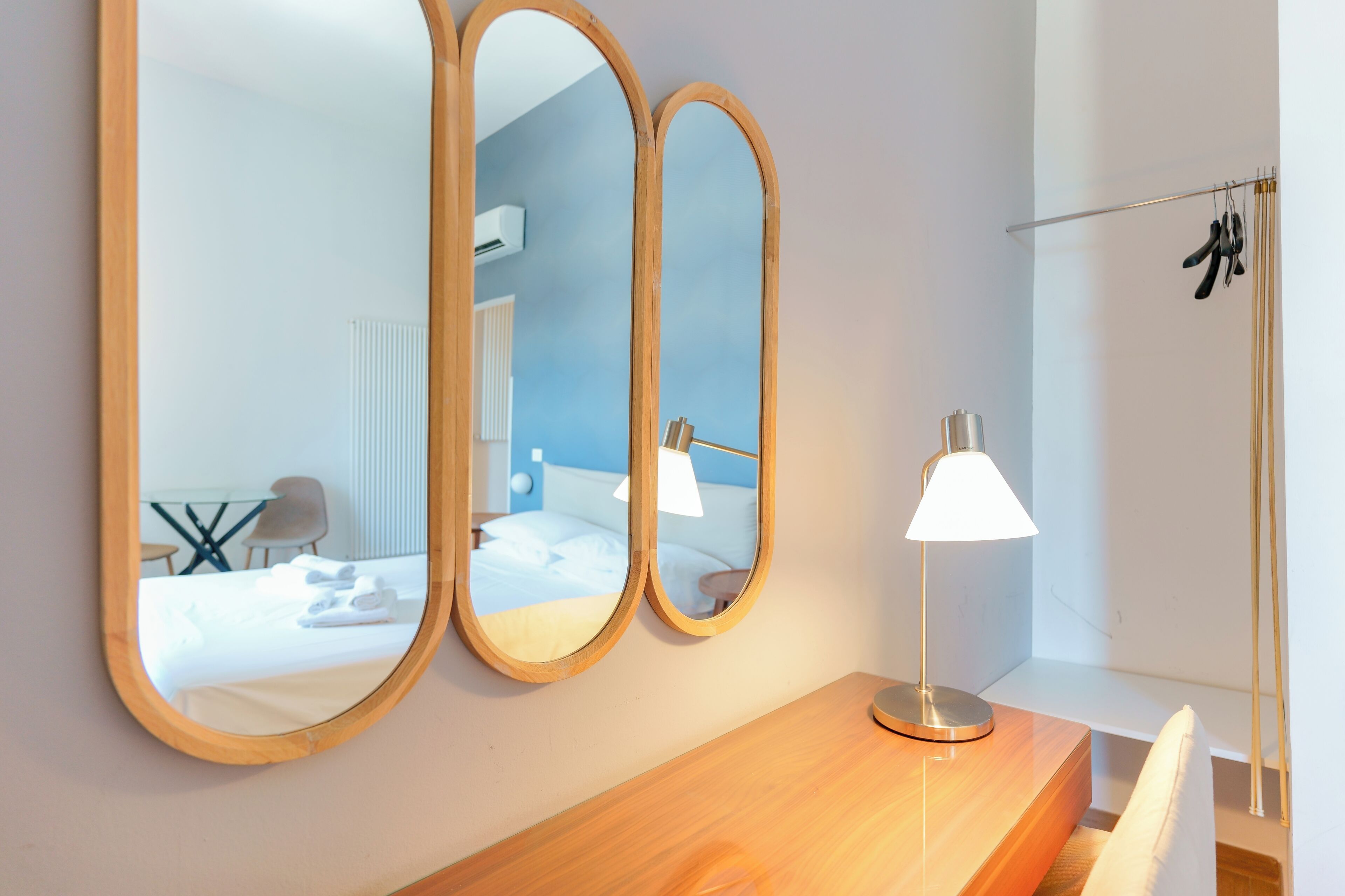 A hotel room with a wooden desk, a lamp, and three mirrors on the wall.