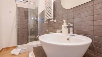 A modern bathroom with a glass shower enclosure, a white sink with a soap dispenser, and a toilet.