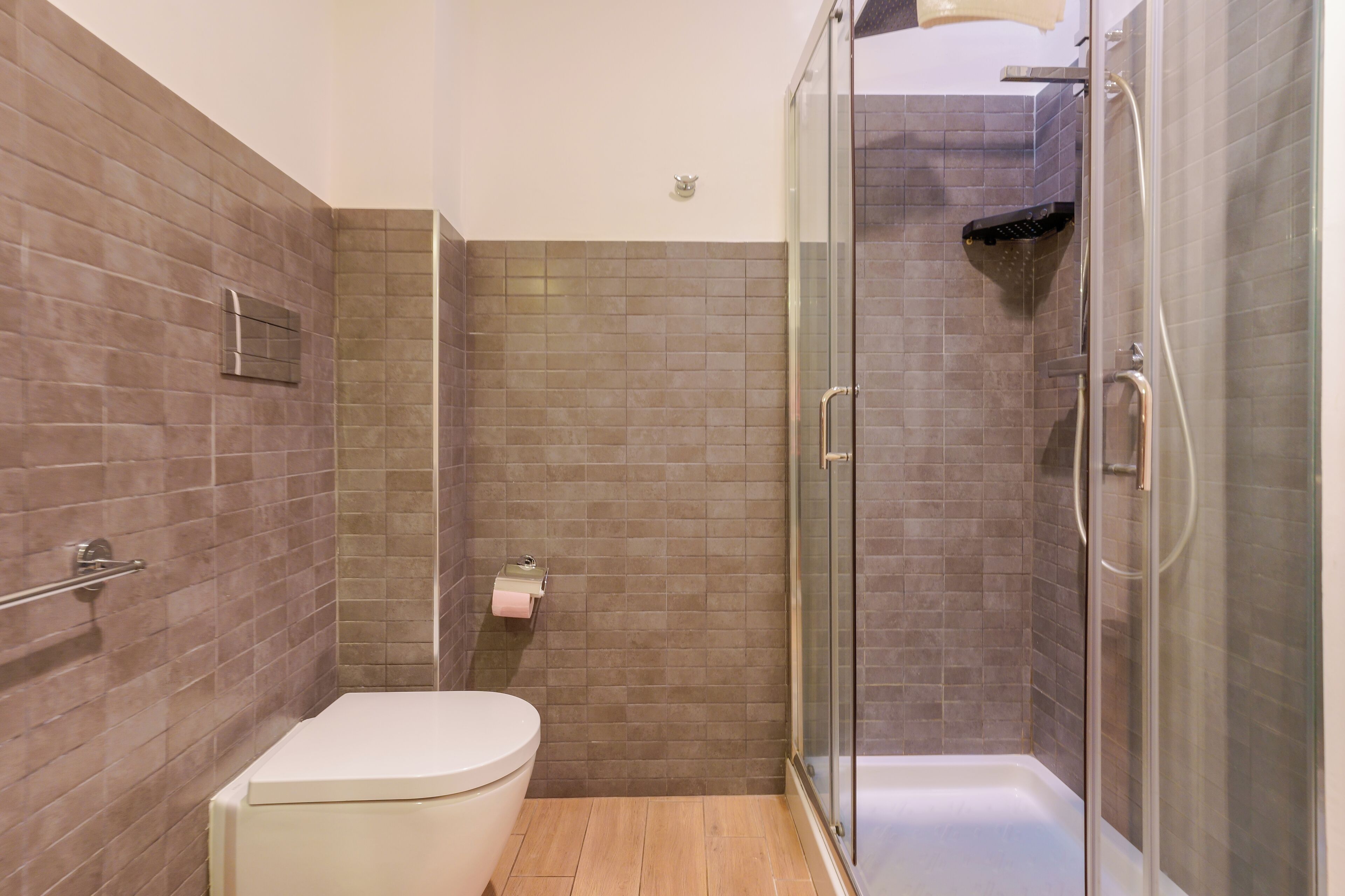 A bathroom with a toilet, a glass shower enclosure, and tiled walls.