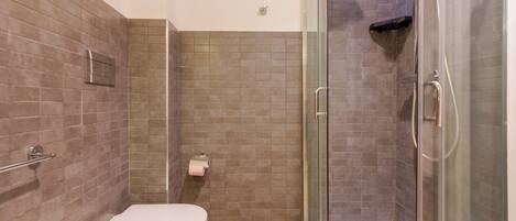 Un baño con inodoro, cabina de ducha de vidrio y paredes de azulejos.