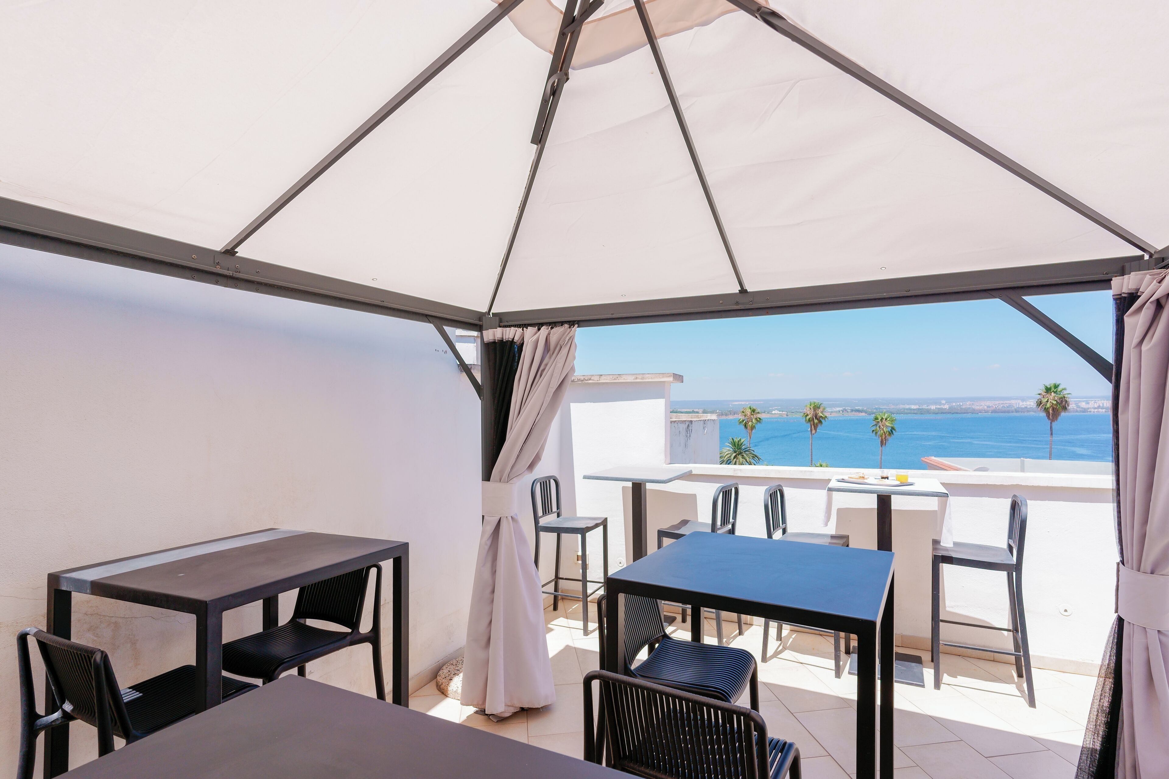 Une terrasse avec une table et des chaises, un auvent blanc et une vue sur la mer.