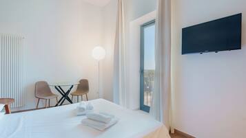 A hotel room with a bed, a desk with chairs, a flat-screen TV mounted on the wall, and a window with curtains.