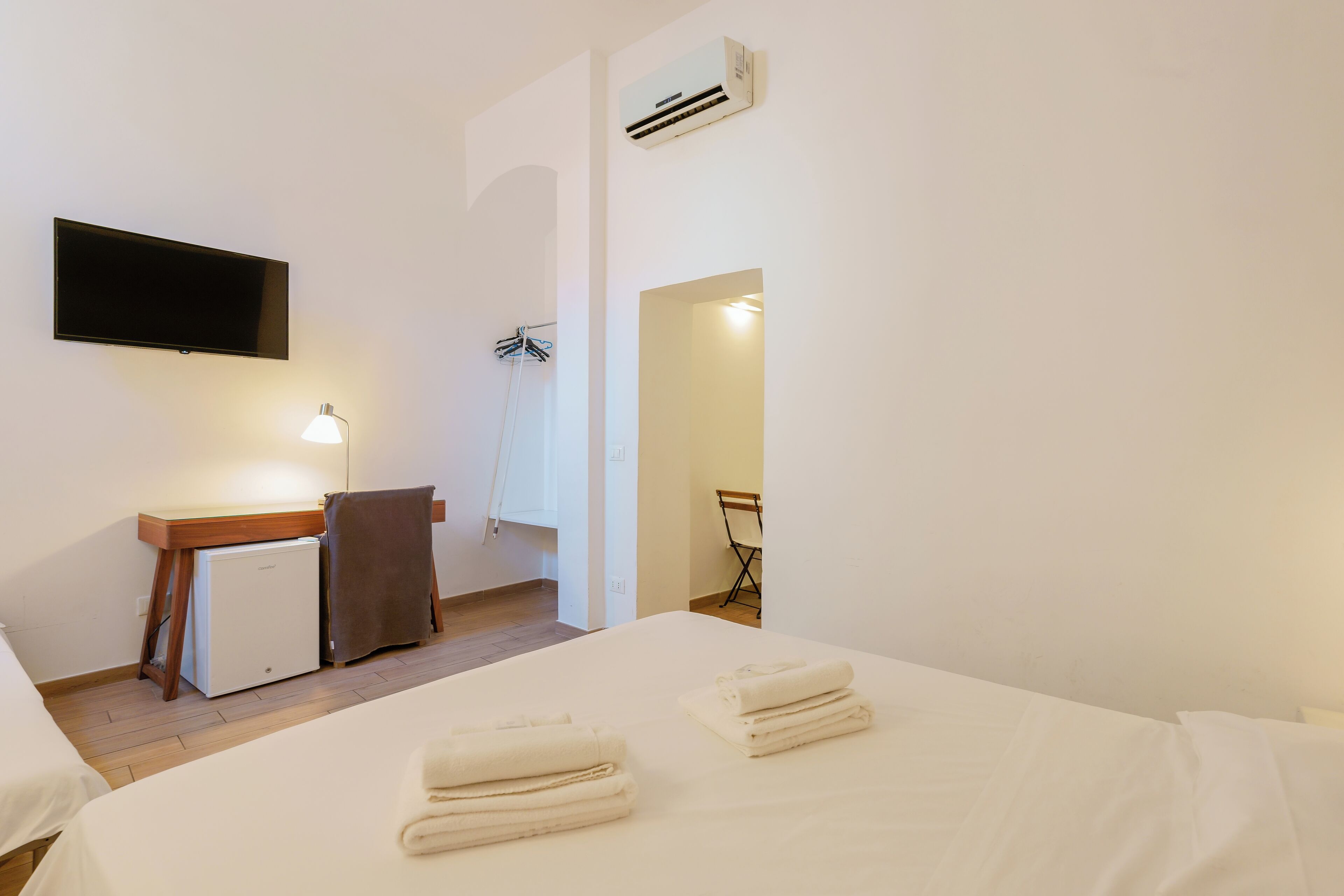 A hotel room with a bed, a desk with a lamp, a TV, and an air conditioner.