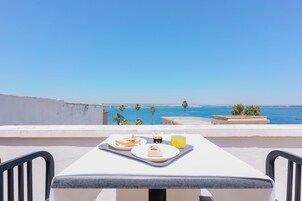 Una terraza con una mesa lista para el desayuno, con vista al mar, palmeras y la costa.