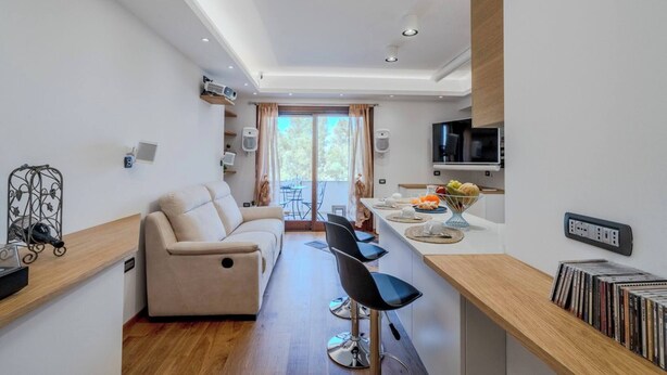 Een moderne woonkamer met een bank, een eethoek met tafel en stoelen, een keuken met televisie, en een balkon met uitzicht.