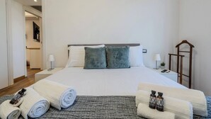 Een netjes ingerichte hotelkamer met een groot bed, twee kussens, een nachtkastje met een lamp, een kleine plant en een houten ladder.
