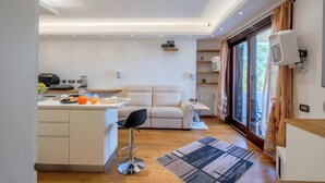 Een moderne keuken met een centraal eiland, een zithoek met een bank en een stoel, en een groot raam met gordijnen.