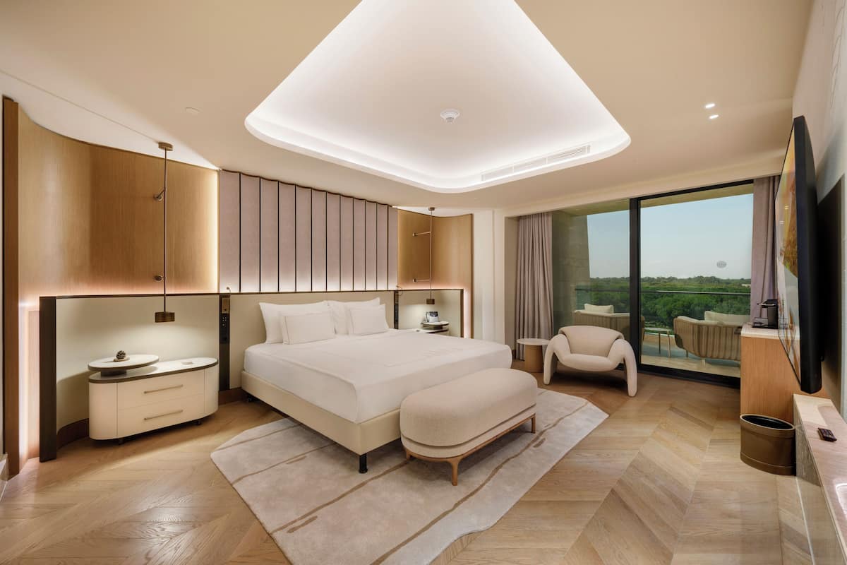 Ein modernes Schlafzimmer mit einem großen Bett, Nachttischen, einer Sitzecke und Blick ins Freie.