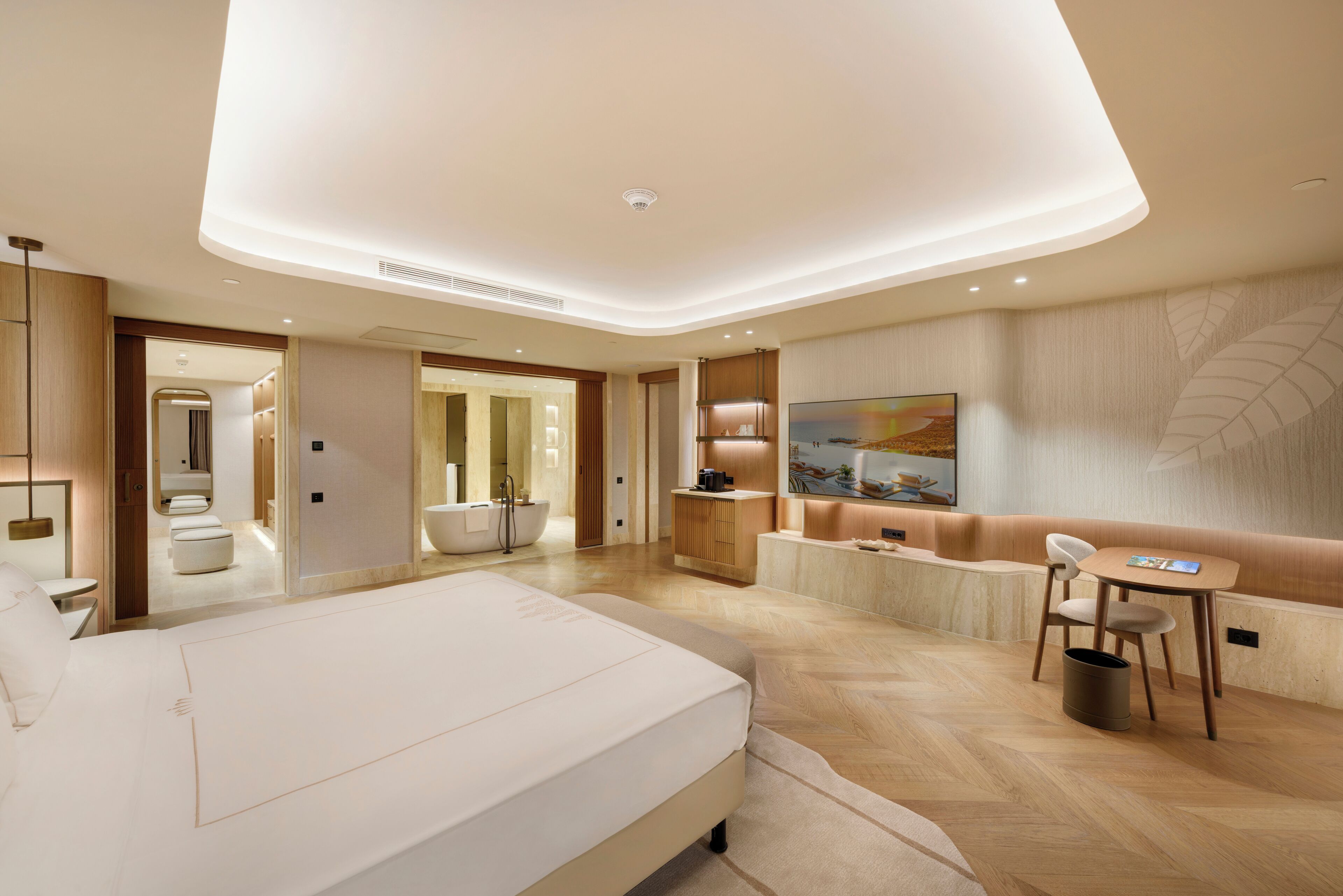 A modern hotel room with a large bed, a seating area with a table and chairs, a TV, and a bathroom with a bathtub and shower.
