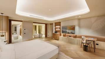 A modern hotel room with a large bed, a seating area with a table and chairs, a TV, and a bathroom with a bathtub and shower.