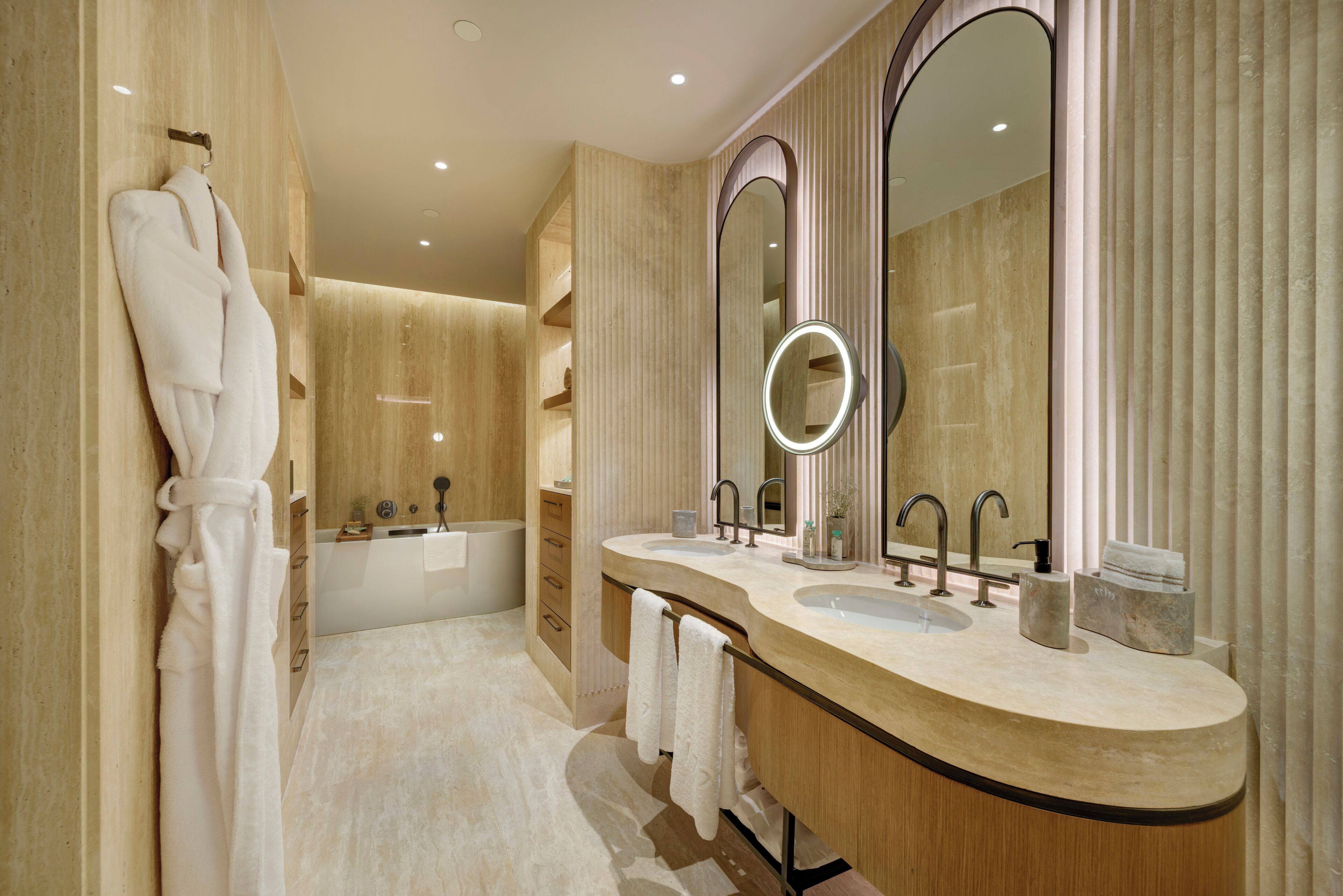 A modern bathroom with a double sink vanity, a large mirror, and a robe hanging on the wall.