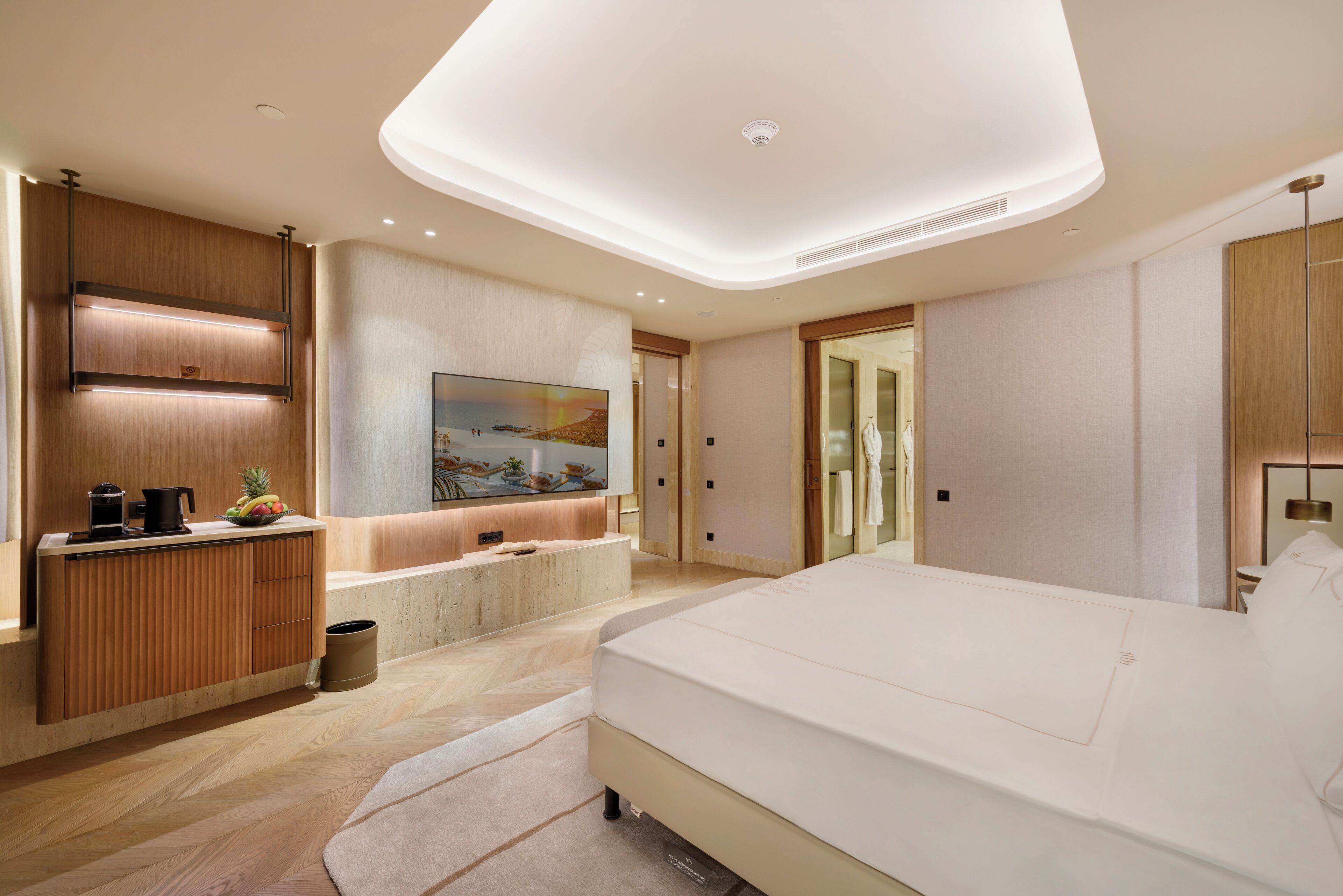 A modern bedroom with a large bed, a built-in desk, a bathtub, and a television.