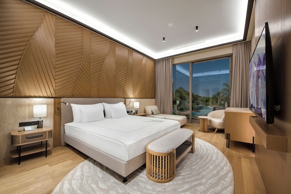 A modern hotel room with a large bed, bedside tables, a desk, a chair, a TV, and a view of the outdoors.