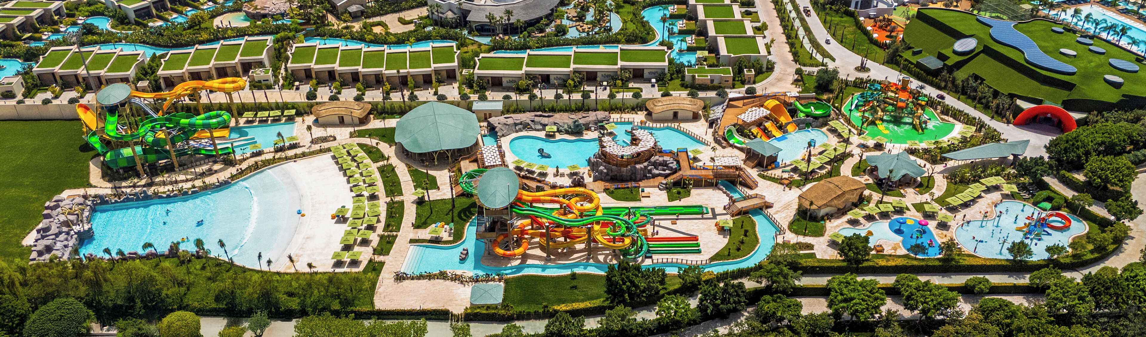An aerial view of a resort with multiple swimming pools, water slides, and a beach area.