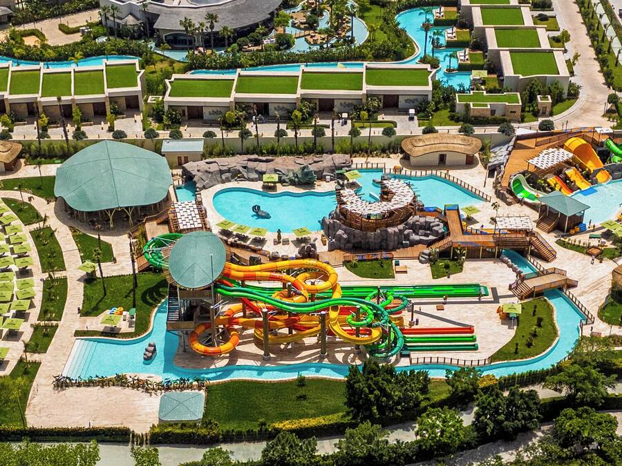 An aerial view of a resort with multiple swimming pools, water slides, and a beach area.