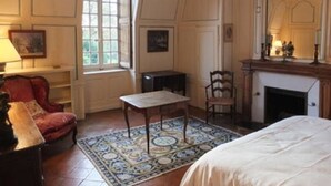 A traditional room with a bed, a fireplace, a small table, and a red armchair. - Historic cottage in charming castle near Le Mans (Saint-Pavace)