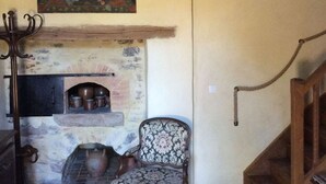A rustic interior with a stone fireplace, a wooden chair, and a painting above the fireplace. - Historic cottage in charming castle near Le Mans (Saint-Pavace)