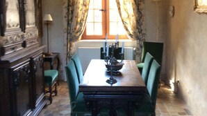 A dining room with a wooden table, green upholstered chairs, a candelabra, and a window with floral curtains. - Historic cottage in charming castle near Le Mans (Saint-Pavace)