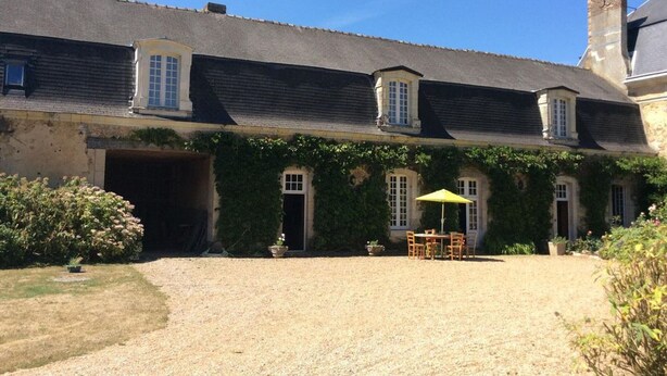 A two-story building with a gravel driveway, a covered patio area with a table and chairs, and a garage entrance. - Historic cottage in charming castle near Le Mans (Saint-Pavace)