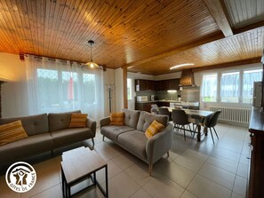 Una sala moderna con sofá y sillón, comedor y cocina.