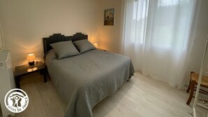 A bedroom with a bed, bedside lamps, a painting on the wall, and a window with curtains.