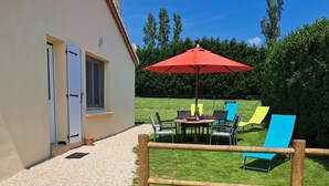 A patio area with a table and chairs, a red umbrella, and a wooden fence.