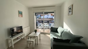 A living room with a TV, a sofa, a coffee table, and a balcony with a view of buildings.