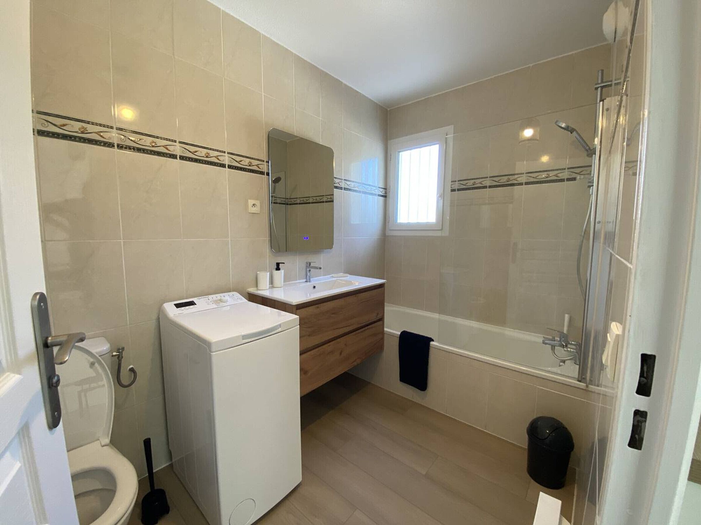 A modern bathroom with a toilet, washing machine, vanity, and shower.