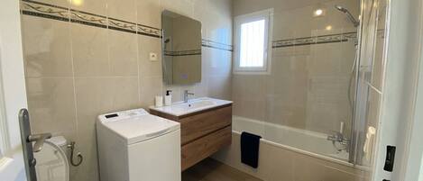 A modern bathroom with a toilet, washing machine, vanity, and shower.