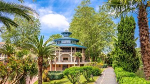A traditional-style building with a blue roof, surrounded by lush greenery and palm trees.