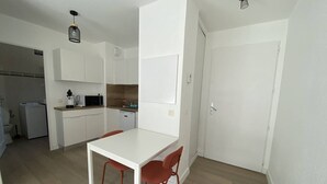 A compact kitchen with white cabinets, a microwave, and a sink. There is a dining table with two chairs.