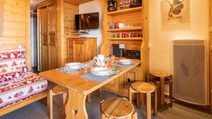 L’intérieur est en bois et comprend une table à manger pour quatre personnes, un téléviseur fixé au mur au-dessus de la table, et un réfrigérateur placé à droite.