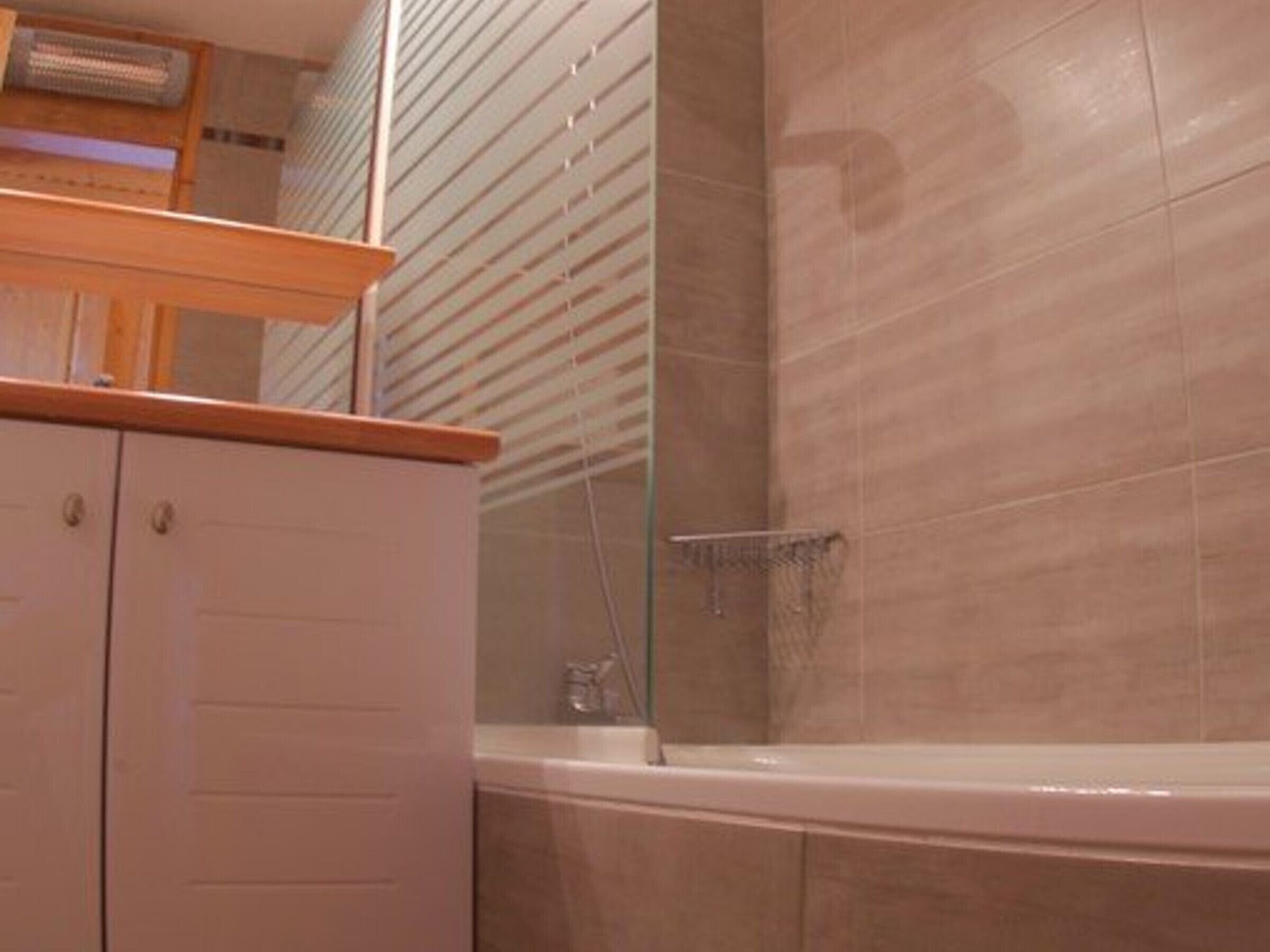 A bathroom with a bathtub, a wooden cabinet, and a glass shower enclosure.