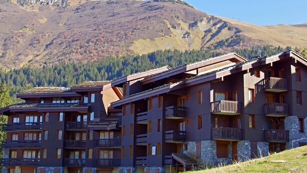 Un hôtel à plusieurs étages, doté de balcons, situé dans un cadre montagneux.