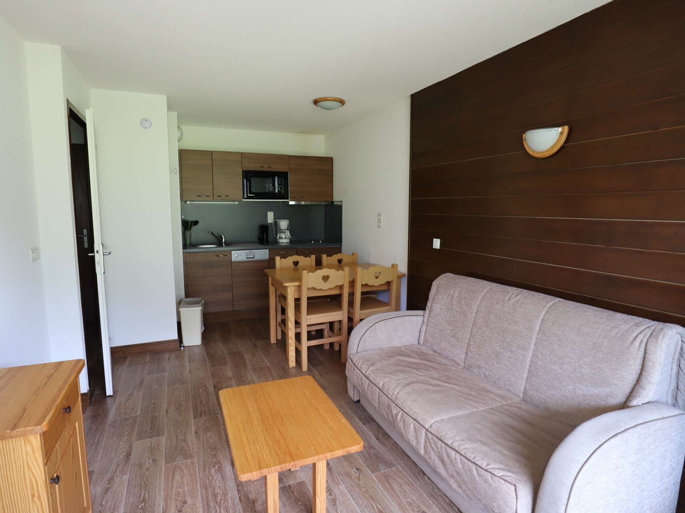 A compact living space with a sofa, a small wooden table, a kitchen area with a microwave, and a wooden wall panel.