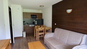 Un espacio habitable compacto con sofá, una pequeña mesa de madera, una zona de cocina con microondas y un panel de pared de madera.