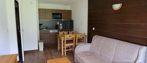 A compact living space with a sofa, a small wooden table, a kitchen area with a microwave, and a wooden wall panel.