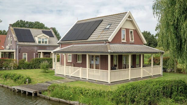 Et hus med en overdækket veranda og solpaneler på taget, beliggende ved en kanal.
