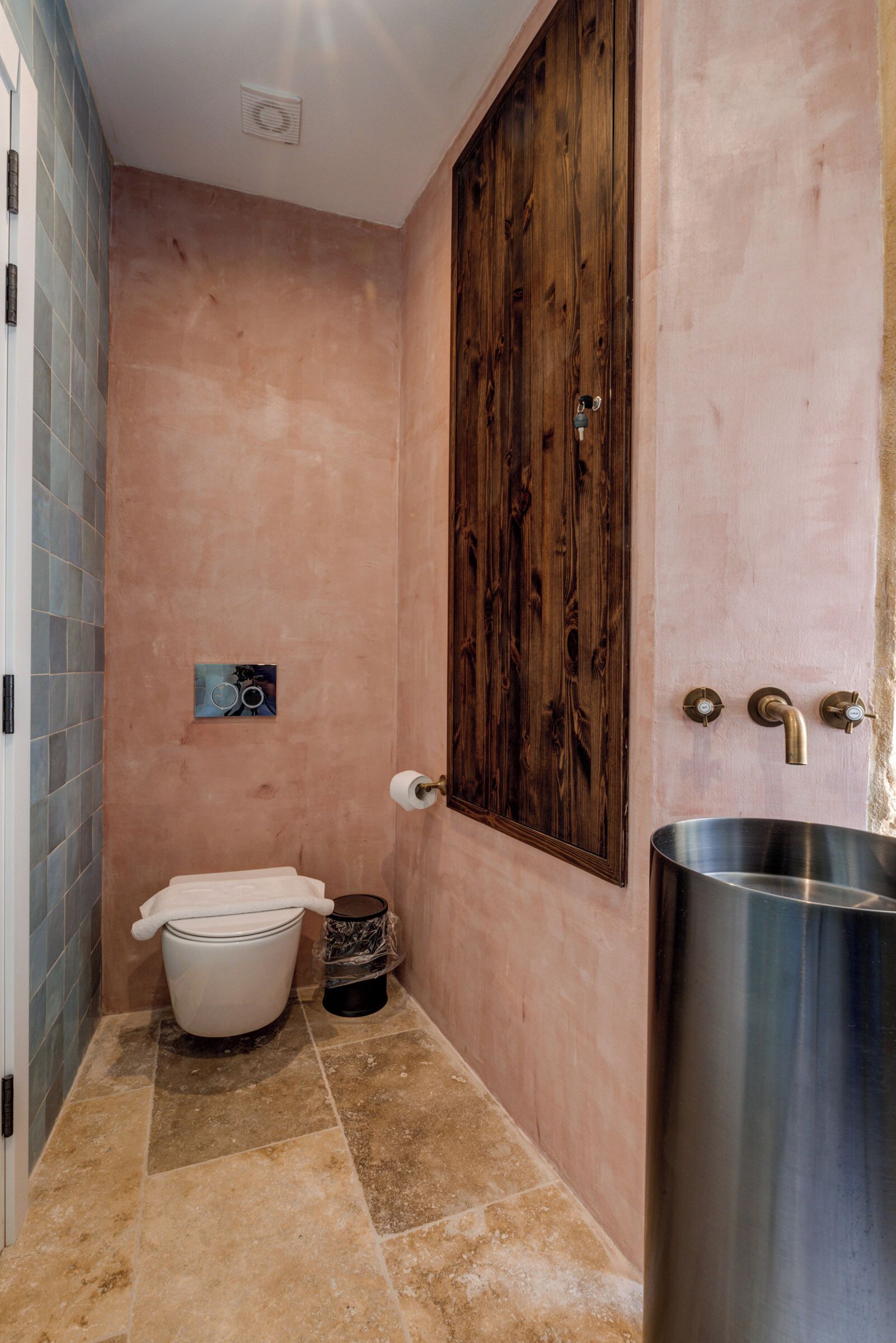 Un bagno con una porta di legno massiccia, un water bianco, un lavandino in acciaio inox e un piccolo cestino.